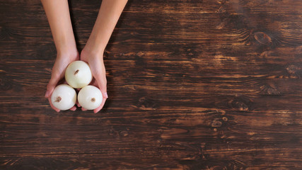 Unrecognizable woman holding vegetables over the wooden table. Close up female hands with onion