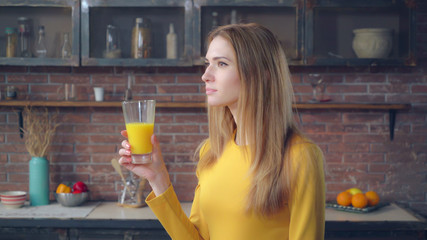 Portrait happy woman drinking orange juice in kitchen. Smiling redheaded lady relishing drink in...