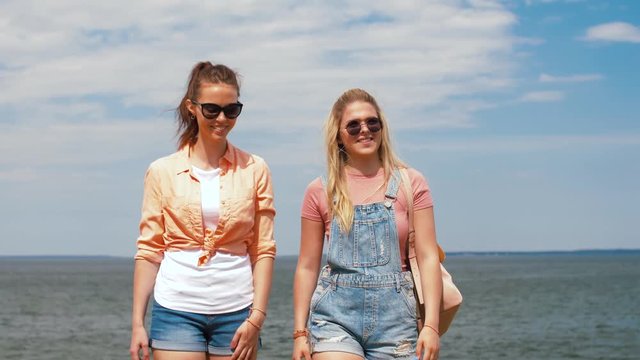 leisure and friendship concept - happy smiling teenage girls or friends walking at seaside in summer