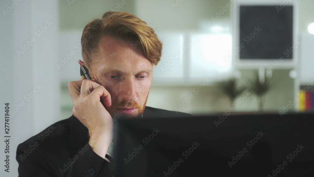 Poster Red-haired man sitting at a computer and calling on the phone. UHD