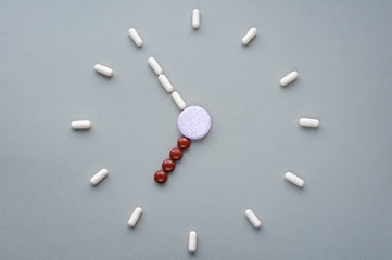Clock created from white pills and brown tablets on green background. Right time for using...