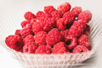 Close-up ripe juicy and delicious raspberry in a plastic transparent dish on a light background. Saturated healthy food