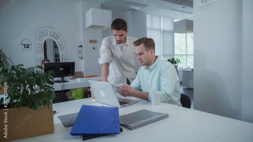 Poster caucasian man sits at the working place and drink coffee. mixed race male comes to the office. men g