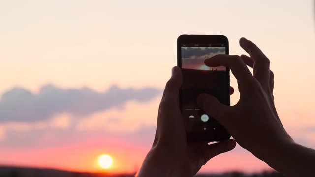 A man taking pictures of the sunset and sky on a smartphone, close-up