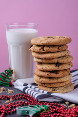 American chocolate cookies, a glass of milk and Christmas decorations. Dark wooden table and pink background. Cookies for the New Year.
