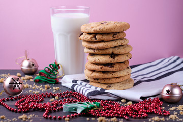 American chocolate cookies, a glass of milk and Christmas decorations. Dark wooden table and pink background. Cookies for the New Year.