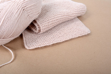 A skein of wool and a knitted scarf of beige thread.