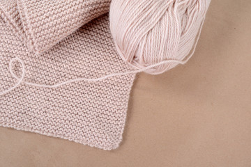 A skein of wool and a knitted scarf of beige thread.