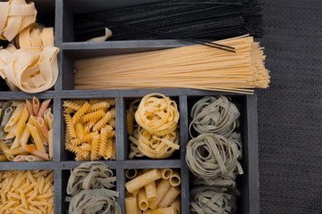 Various mix of pasta on wooden rustic background, wood desk and wooden box.