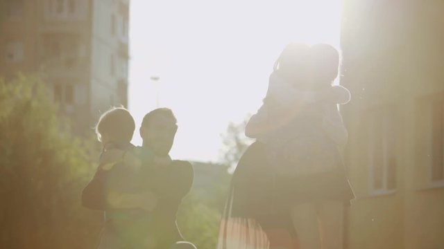 Adorable family hugs under sunset. View of happy parents and their school children meeting together after school in lovely weather.