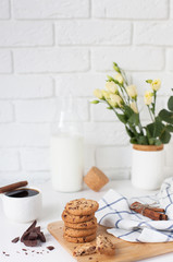Fototapeta na wymiar Morning breakfast with hot ground coffee with cinnamon, sweet pastry with chocolate, a bottle of fresh milk and a bouquet of beautiful flowers in a vase against a white brick wall