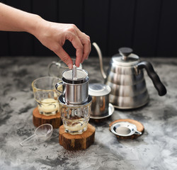 Making pour over Vietnamese milk coffee. Woman hand pressing coffee in phin on dark background