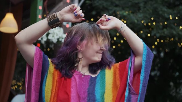 bright hipster girl is crazy dancing and singing outdoors. portrait of a young woman with colored hair and body piercing.