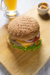 Burger with beef patty, salad, a slice of tomato and cheese, onions and sauce with paprika in a grilled bun with sesame