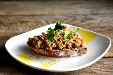 Chicken liver pate sandwich in a white plate on a wooden table.