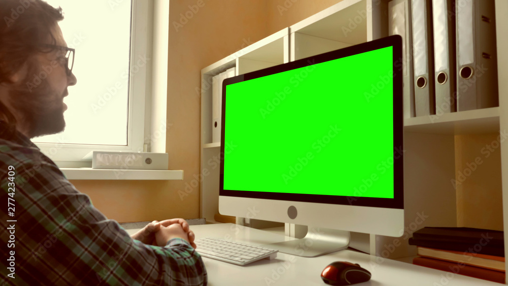 Aufkleber man sitting at workplace paying game on computer in small office. businessman with beard looking on display with green screen. employee in startup company typing on keyboard use pc mouse