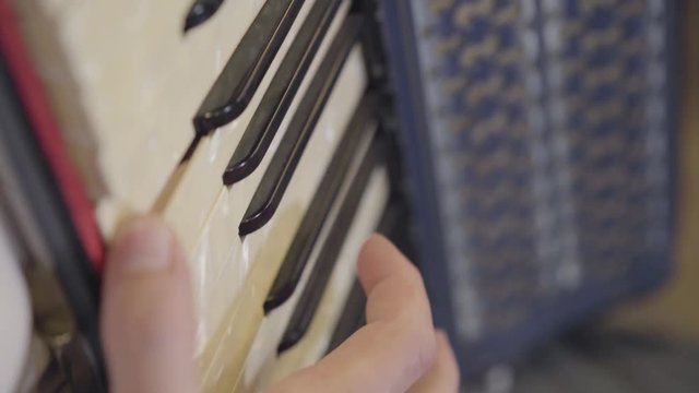 The hand of an unrecognized man playing the keys of the button accordion close-up.