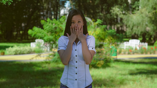 portrait asian woman frightened. Afraid young girl standing in front of green tree outdoors. Her long black hair shine on the sun. Vietnamese female wearing in casual t-shirt smiling looking at the