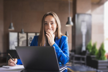 Business woman with laptop and notebook looks thoughtfully