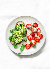 Healthy snack, breakfast - sandwich with avocado and fresh strawberries on a light background, top view