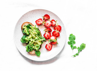 Healthy snack, breakfast - sandwich with avocado and fresh strawberries on a light background, top view