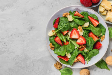 bowl of summer spinach salad with strawberry, parmesan cheese and walnuts on concrete background. healthy diet food