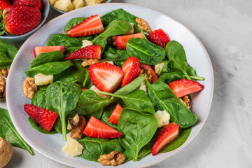 salad with strawberry, spinach leaves, parmesan cheese and walnuts on concrete background. healthy diet food