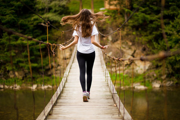 Tourist woman walk by long wooden suspension bridge above river.