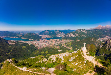Beautiful panoramic sunrise landscape at town Lecco, lake Como in sunny summer day. Stunning airial view to cross on top of mountain from drone near viewpoint Piani (Pizzo) d'Erna, alps, italy, Europe