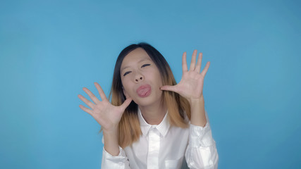 young asian woman posing have fun making faces on blue background in studio. attractive millennial girl wearing white casual shirt looking at the camera smiling