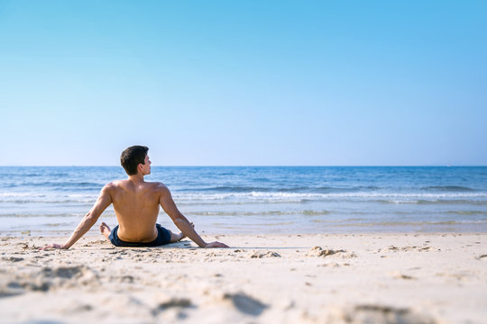 Young man on beach lying in sand looking at the ocean. Young male model enjoying summer travel holiday by the sea. Happy vacation relaxing concept