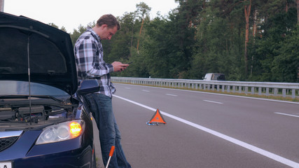 Handsome man stuck on the side of the road with a flat tire using smartphone surfing internet or use app or messaging.