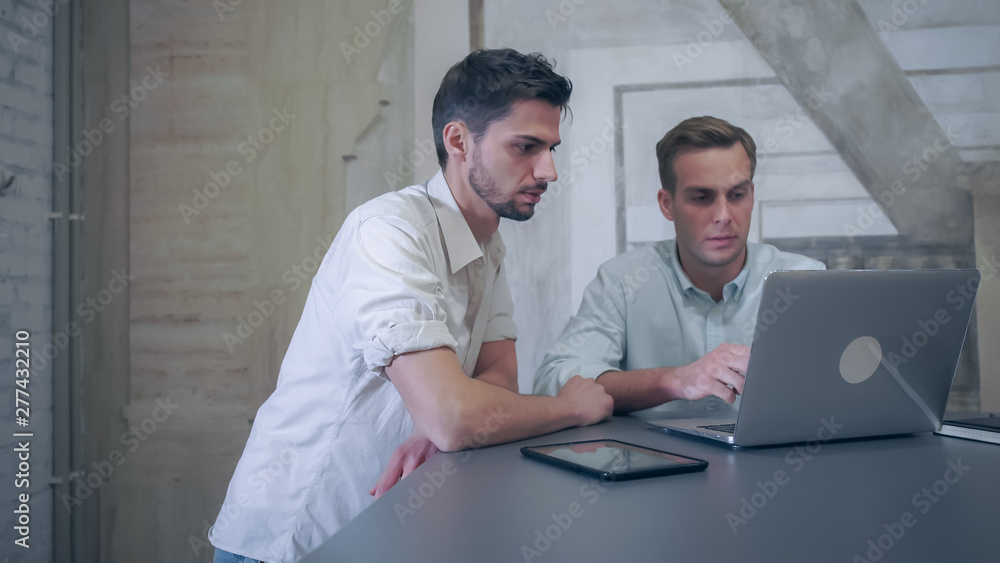 Aufkleber one man sits by the big grey table. another male comes to the working place. businessmans work with 