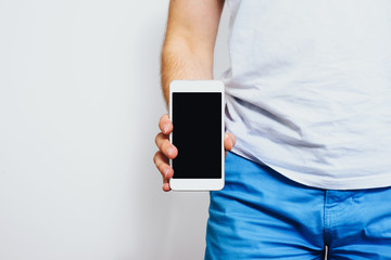 Phone in hand with a blank screen. A man wearing a white T-shirt is holding a phone with a blank display. Content completion concept.