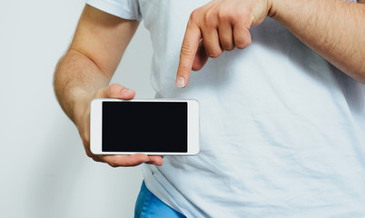 Phone in hand with a blank screen. A man wearing a white T-shirt is holding a phone with a blank display. Content completion concept.