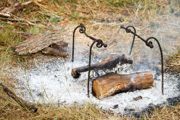 Extinguished fire with burnt wood near the metal racks for cooking