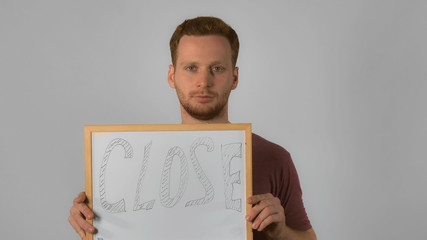 happy caucasian guy with red hair posing showing whiteboard with handwriting close. handsome redhead men wearing in casual t-shirt. Portrait young caucasian man on grey background