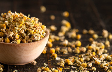 A Bowl of Dried Chamomile Flowers Spilled on a Dark Wooden Table