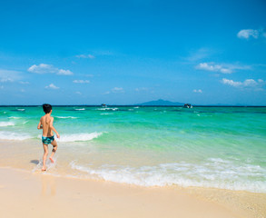 Fototapeta na wymiar Young boy running on beach looking at the blue ocean. 
