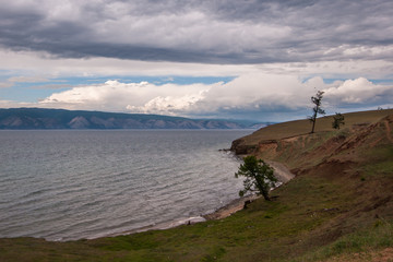 Baikal lakeside with mountains in the background and beautiful clouds. Trees on the lake shore. Lake with waves.