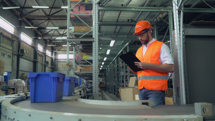 Manager checking delivery and inventory. Man standing near packaging line writing some information....