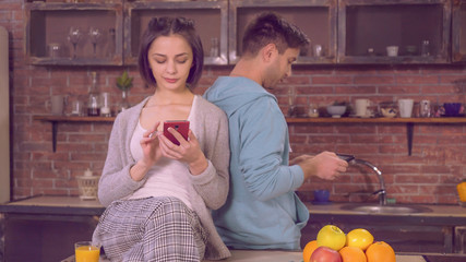 family in the evening using modern device at home. Young woman sitting on the table in kitchen. Lady wearing in sleepwear using smartphone drinking orange juice. Happy couple in love have fun at home
