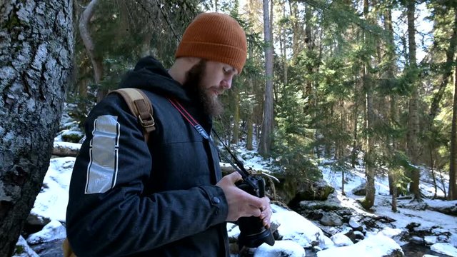 A bearded male traveler photographer with his camera in the winter forest takes pictures of nature. Travel concept for bloggers and photo artists