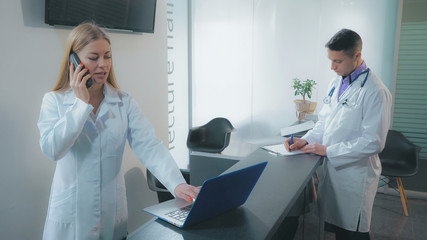 Doctor giving nurse patient s medical record. Adult professional therapist holding tablet fill documents using touch screen in clinic. Man wearing in white coat.