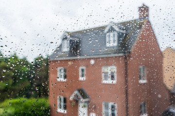 Detached red family house viewed through a glass window covered in rain water drops - 277437623