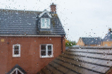 Glass window covered in rain water drops with view of house and roof in the background