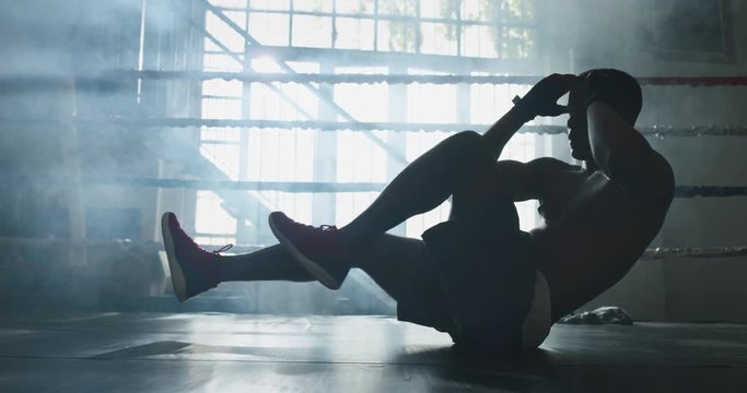 Cinematic shot of a professional young muscular shirtless african man is practicing shadow boxing work out in a gym with ring.