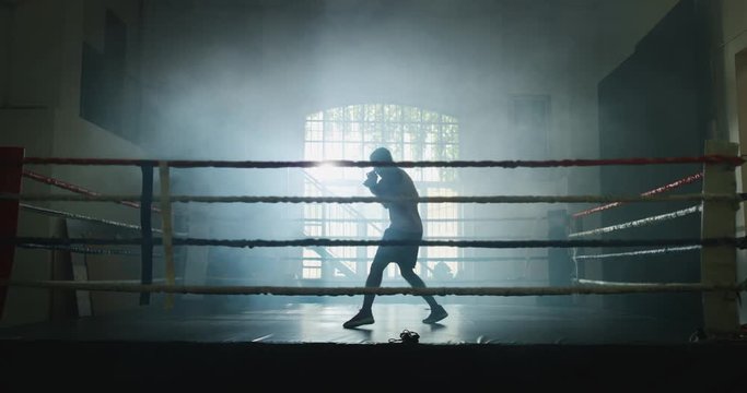 Cinematic slow motion shot of a professional young muscular african man is practicing shadow boxing work out in a ring. 