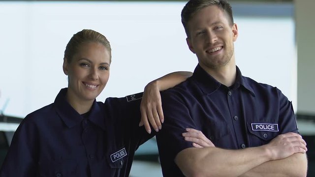 Happy police teammates smiling into camera, patrolling city, reliable service