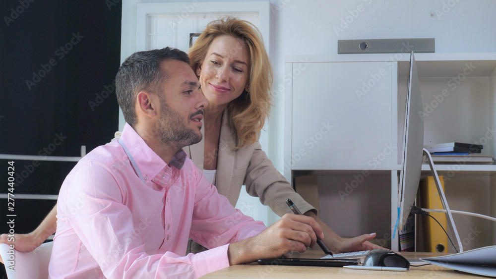 Aufkleber Two designers talking about project. Handsome man drawing using digital tablet near standing caucasian woman looking on display computer with happy smile